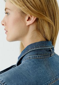 Jeansjacke mit einem strukturierten Kragen, mittlerer Waschung und sichtbaren Nähten. Das Design hat eine klassische Passform und eine weiche Textur.