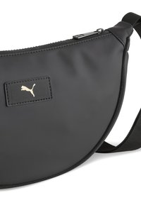 Black sling bag in smooth material with a zip closure, featuring a gold Puma logo patch and adjustable black strap. Rounded design.