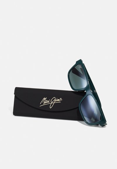 Teal sunglasses with gradient gray lenses, angular design, and logo on the side, placed beside a black protective case with gold lettering.