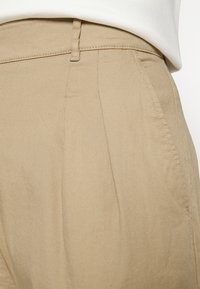 Beige broek van gestructureerde stof, met een getailleerde pasvorm, zijzakken en zichtbare stiksels langs de tailleband en naden.
