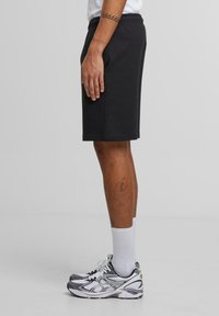 Man wearing black shorts, white ribbed socks, and white-gray running shoes standing sideways on a plain gray background.