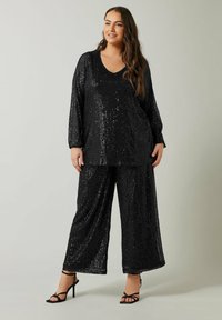 Haut en sequins noir avec un décolleté en V et des manches longues associé à un pantalon large noir. Les deux pièces présentent une texture scintillante et une coupe ample.