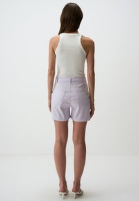 Shorts en denim violet clair avec une taille ajustée, deux poches arrière et un design épuré et soigné. Associés à un débardeur blanc à côtes.
