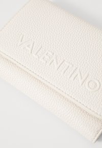 Portefeuille en cuir texturé blanc avec le logo "VALENTINO" embossé sur le devant, à design rabattu et avec des détails de couture visibles.