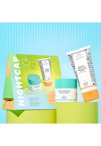 Nightcap set featuring two skincare products: a white tube with black accents, a turquoise jar, and a cream with an orange lid, all on green packaging.