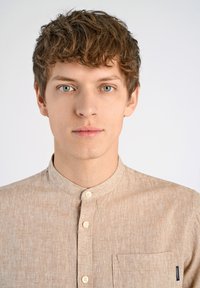 Camicia beige con colletto in tessuto testurizzato, dotata di una patta frontale con bottoni e una tasca applicata sul lato sinistro.