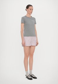 Camiseta de algodón gris con logo blanco de "MAX", combinada con pantalones cortos a rayas rosas y blancas. El modelo lleva calcetines grises y zapatos negros.