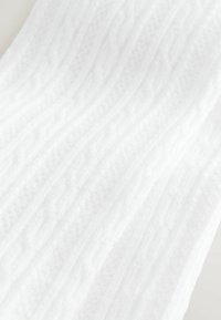 Valge kootud kangas tekstuurse palmiku mustriga, millel on reljeefsed kujundid ning pehme ja sile väljanägemine.