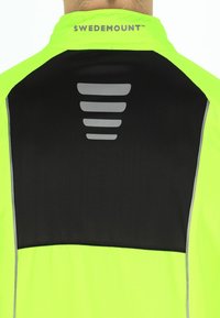Fluorescerende gul atletisk jakke med en sort bagpanel, der har et tekstureret stribe-design i grå og reflekterende detaljer på ærmerne.