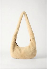 Bēšas krāsas kažokādas rokassoma ar unikālu izliektu rokturi. Mīksta tekstūra, noapaļota silueta un minimālistisks dizains bez redzamas metāla detaļas.