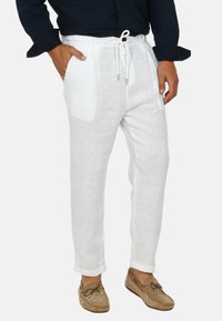 I pantaloni bianchi in lino hanno una vestibilità rilassata, una vita elastica con cordoncino, tasche laterali e orli arrotolati. Abbinati a scarpe marrone chiaro.