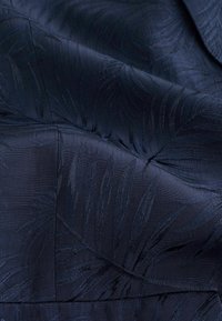 Marinblått tyg med ett texturerat bladmönster. Materialet har en slät lyster, med subtila variationer i texturen som skapar djup.