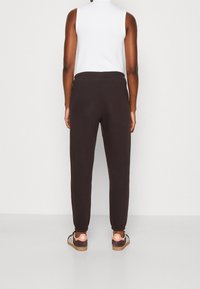 Joggers marrón oscuro con una textura suave, cintura elástica y puños ajustados, combinados con zapatillas marrones y rosas. Diseño minimalista.