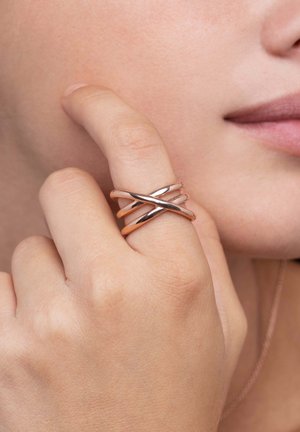 Drei miteinander verwobene Ringe aus poliertem Roségoldmetall, die ein elegantes Design mit glatten Oberflächen aufweisen. Nahaufnahme, getragen an einem Finger.
