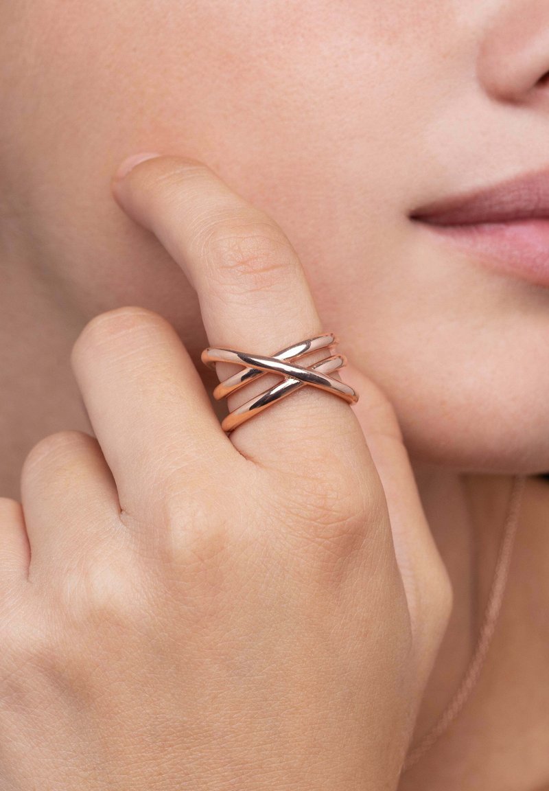 Tre anelli intrecciati in metallo oro rosa lucidato, caratterizzati da un design elegante con superfici lisce. Indossati su un dito, vista ravvicinata.
