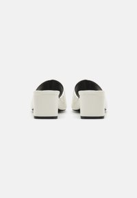 White block-heeled mules with a smooth leather finish and open back design, featuring a subtle black accent at the heel base.