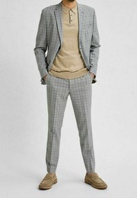 Šedý károvaný oblek s upraveným střihem, lehkou texturou, doplněný béžovým polo tričkem a béžovými semišovými mokasíny.