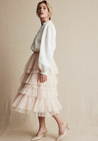 Hvid broderet bluse med pufærmer, parret med en lagdelt, tiered blush tulle nederdel og nude hæle.