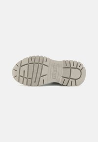 Sole di sneaker grigia chiara con una superficie in gomma testurizzata, caratterizzata da profonde scanalature per una migliore trazione e un dettaglio del logo rialzato al centro.
