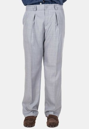 Pantaloni da abito plissettati grigio chiaro indossati con mocassini in camoscio marrone, abbinati a una camicia blu scuro infilata dentro.