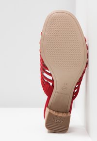 Sandale rouge à brides avec semelle beige montrant un dessous texturé antidérapant et un petit talon en bois, taille 37.