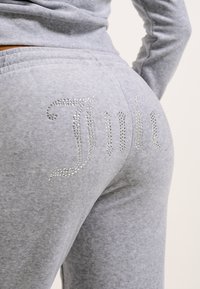 Szürke, puha anyagú melegítőnadrág, melynek hátsó részén gyöngyökkel kirakott "Juicy" felirat található, illeszkedő és szűkített fazonnal.