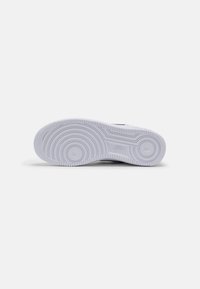 Semelle blanche de basket Nike avec motifs circulaires sur la bande de roulement et logo Nike au centre sur un fond gris uni.