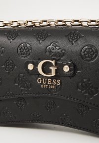Borsa in ecopelle nera con texture, caratterizzata da motivi in rilievo, un logo G in tonalità oro e una tracolla in metallo.