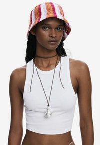 Häkel-Bucket-Hut mit orangefarbenen, rosa und weißen Streifen. Das Model trägt ein weißes geripptes Cropped-Top und eine Silberanhängerkette an einem braunen Band.