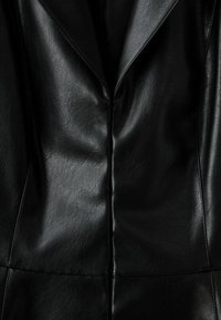 Veste en cuir noire en gros plan montrant la couture avant et les détails du col à revers avec une surface lisse et légèrement texturée.