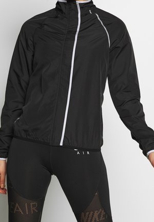 Sort letvægtsjakke med høj krave; har reflekterende hvide detaljer og en glat, blank overflade; parret med sorte leggings.