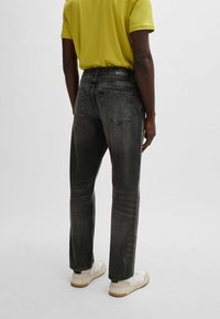 Vaqueros de denim negro con ajuste recto, textura deslavada y cinturilla con marca. Llevados con una camisa amarilla de manga corta y zapatillas blancas.