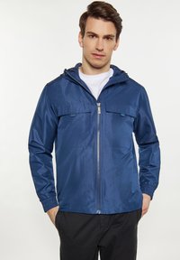 Tamsiai mėlynas lengvas striukė su užtrauktuku, kapišonu ir dviem krūtinės kišenėmis; pagaminta iš lygios, blizgios medžiagos su elastingomis rankovėmis.