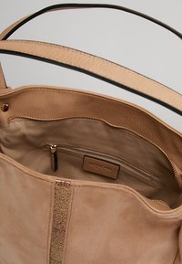 Borsa tote beige con una superficie testurizzata e un interno liscio. Presenta una tasca con zip e dettagli in hardware dorato.
