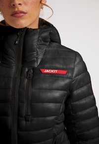 Giubbotto puffer nero con zip frontale, design trapuntato, colletto alto e un patch logo rosso "JACK1T" sul petto. Tessuto testurizzato.