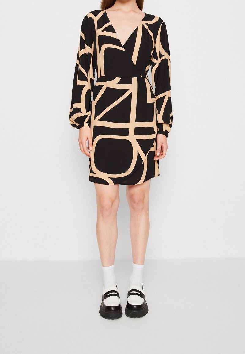 Robe noire avec un décolleté en V et de longues manches bouffantes. Présente un motif abstrait beige en contraste. Associée à des chaussettes blanches et des chaussures noires à semelles épaisses.