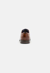 Brown leather shoe featuring a rounded toe, a textured finish, and a contrasting blue fabric lining with a sturdy black heel.