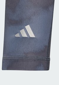 Tmavomodré športové legíny s textúrovaným povrchom, ktoré majú reflexné strieborné logo Adidas na stehne a spevnené švy na leme.