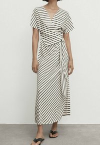 Randig omslagsklänning i kräm och svart. V-ringning, korta ärmar, medellång med en sidbanddetalj. Mjuk, lätt tyg. Svarta sandaler.