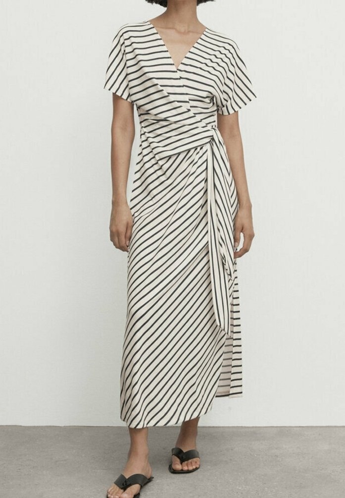 Randig omslagsklänning i kräm och svart. V-ringning, korta ärmar, medellång med en sidbanddetalj. Mjuk, lätt tyg. Svarta sandaler.