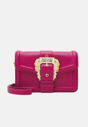 Borsa a tracolla in pelle fucsia con fibbia ornamentale dorata incisa con "Versace Jeans Couture" e tracolla staccabile su sfondo bianco.