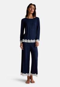 Il set di pigiama blu navy presenta maniche lunghe e pantaloni a gamba larga, decorati con delicati bordi in pizzo bianco lungo l'orlo e i polsini. Tessuto morbido.
