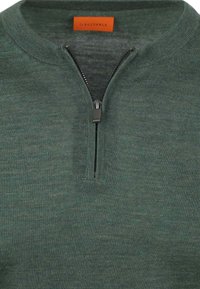 Groene zip-up trui met textuur breiwerk, ronde kraag en contrasterende rits. Het label is oranje en bevindt zich aan de binnenkant bij de hals.