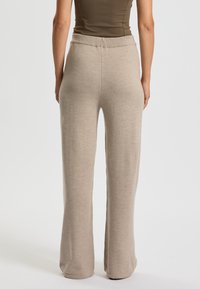 Beige strikkede bukser med vidde, elastisk talje, glat tekstur og fuld længde, set bagfra.