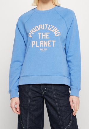 Felpa azzurra chiara realizzata in tessuto morbido, con la scritta arancione "PRIORITIZING THE PLANET" in design ad arco. Collo e polsini a coste.