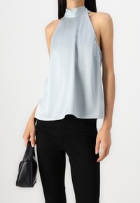 Ljusblå halterneck-topp i strukturerad tyg, med hög hals och lös passform. Kombinerad med svarta byxor och en liten svart väska.