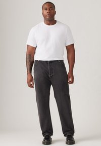 Zwarte denim broek met een relaxed fit, gecombineerd met een eenvoudig wit T-shirt en zwarte schoenen. Gladde textuur, gedetailleerde stiksels en geen zichtbare patronen.