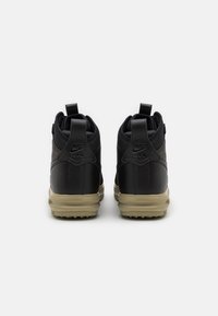 Ett par svarta Nike Air-sneakers visade bakifrån med beige sulor och dragflikar mot en vit bakgrund.