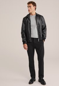 Svart läderbomberjacka med dragkedja fram, grå stickad tröja med rund hals, svarta slim-fit byxor och svarta skor med tofsar.