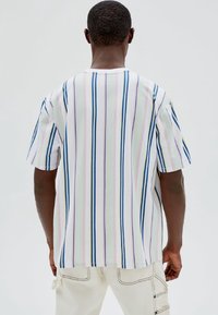 Camisa de manga corta de algodón blanco con rayas verticales en azul, rosa y verde. Corte holgado con escote redondeado y sin logotipos.